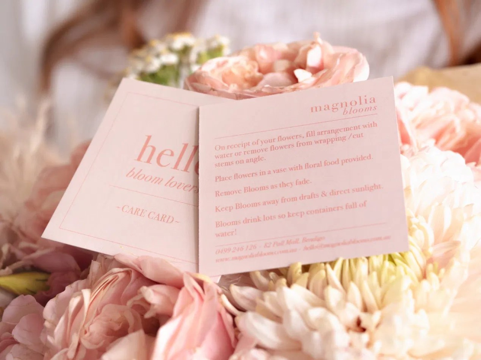 A Magnolia Blooms care card tucked into a bouquet of blush blooms